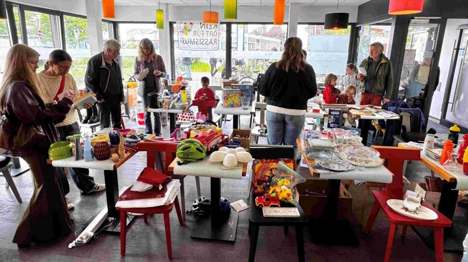 Kostnix Flohmarkt in Brühl-Ost Menschen in einem Café, das mit Tischen und bunten Gegenständen für Kinder gefüllt ist.