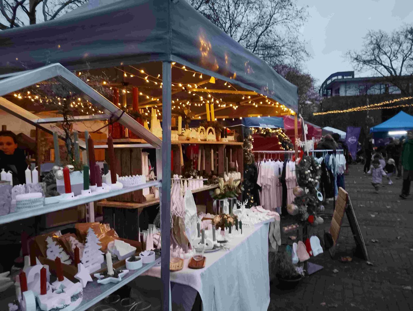 Weihnachtsmarkt Ortsgemeinschaft Brühl-Ost 2025 auf dem Vorplatz St. Stephan Weihnachtsmarktstand mit dekorierten Ständen und Lichtern, umgeben von Besuchern.