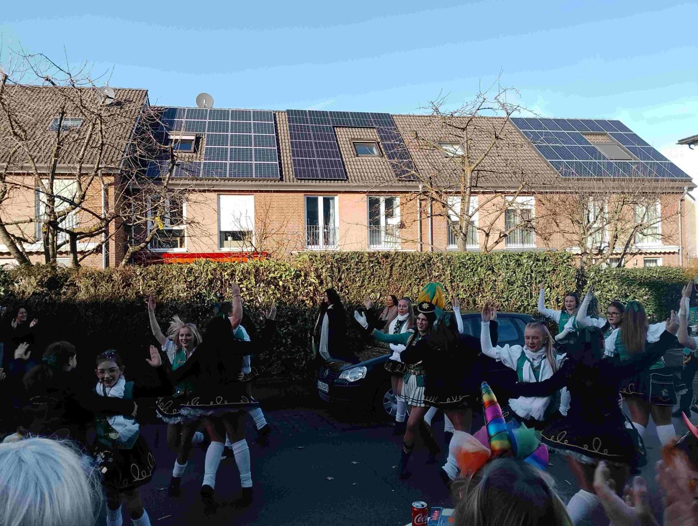 Karnevalszug in Brühl-Ost 2026 Kinder in traditioneller Kleidung tanzen fröhlich in einem Garten. Solarpanels im Hintergrund.