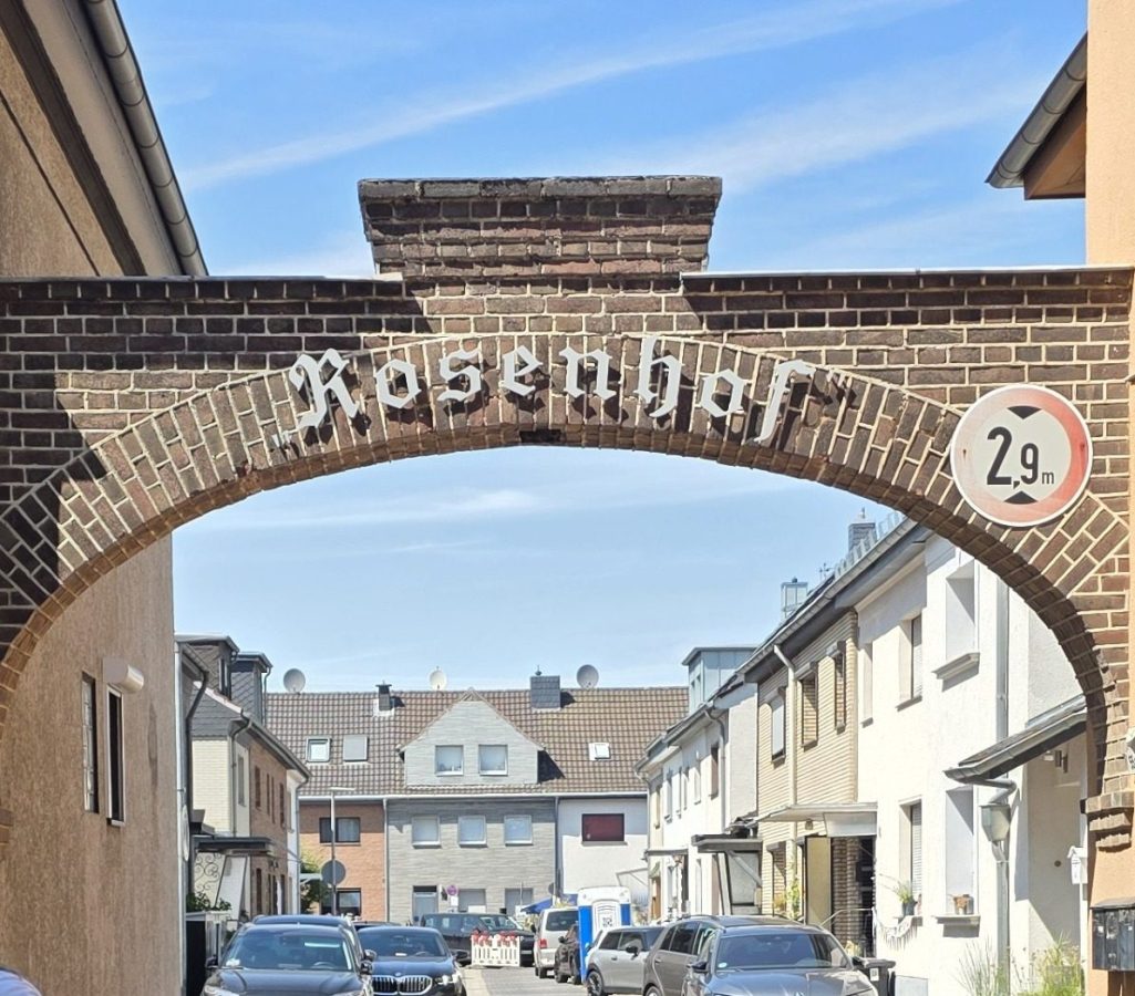 Der Rosenhof in Brühl fiert 2026 sein 100 jähriges Jubiläum Ein historischer Bogen mit der Aufschrift "Rosenhof" über einer Straße.