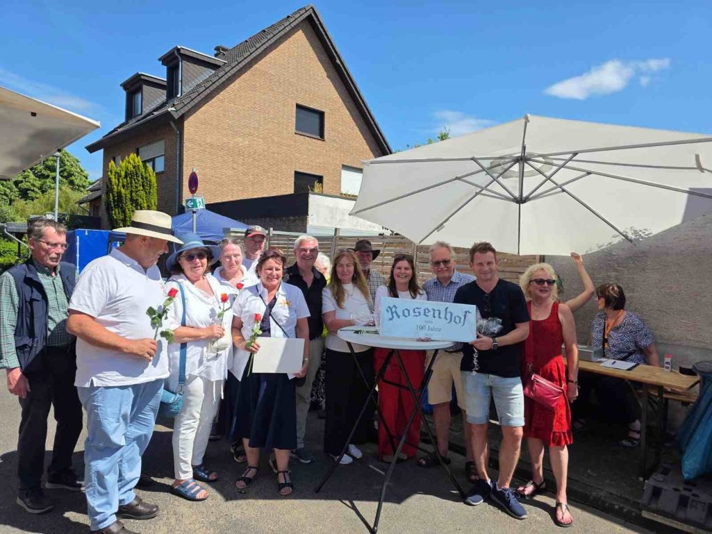 Die Ortsgemeinschaft Brühl-Ost feiert mit beim 100 jährigen Rosenhof Jubiläum 2026 Gruppe von Menschen mit Blumen und einem Schild bei einer Veranstaltung im Freien.