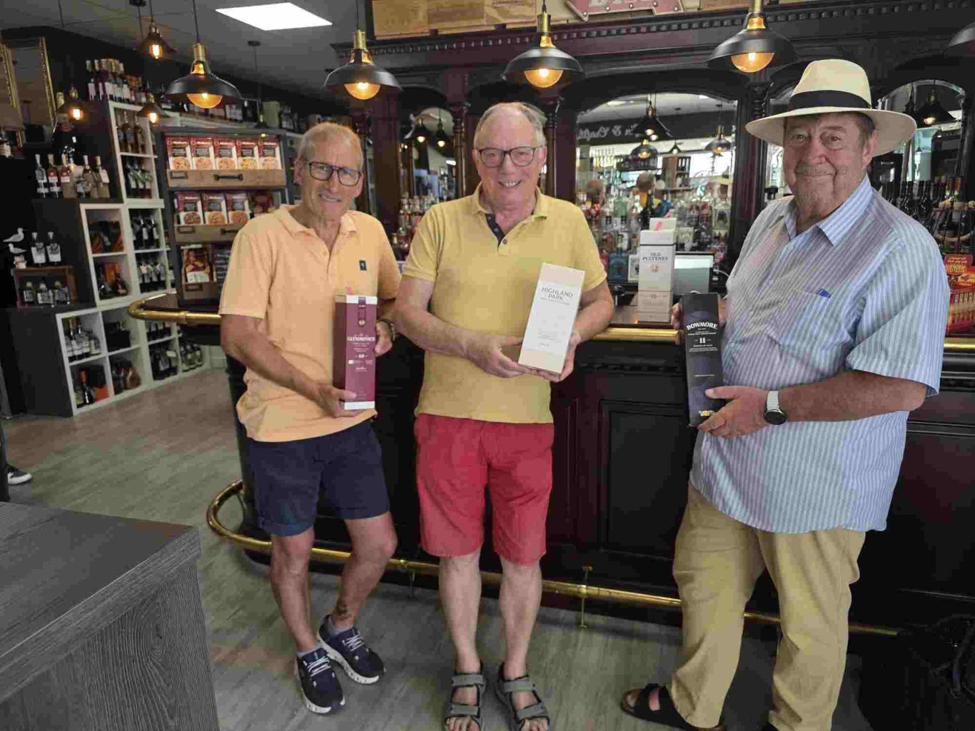 Whisky Tasting in Brühl-Ost Drei Männer in einem Geschäft halten Flaschen in der Hand, lächeln und posieren.