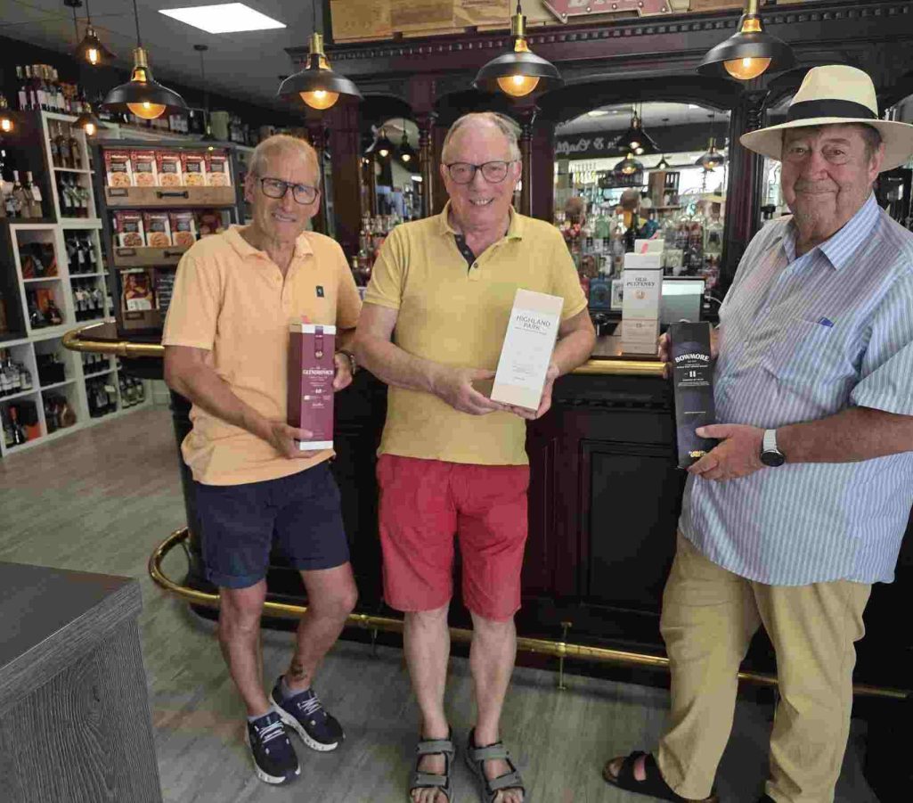 Ortsgemeinschaft Brühl-Ost. Einladung zum Whisky Tasting Drei Männer stehen an einer Theke und präsentieren Flaschen in einem Geschäft.