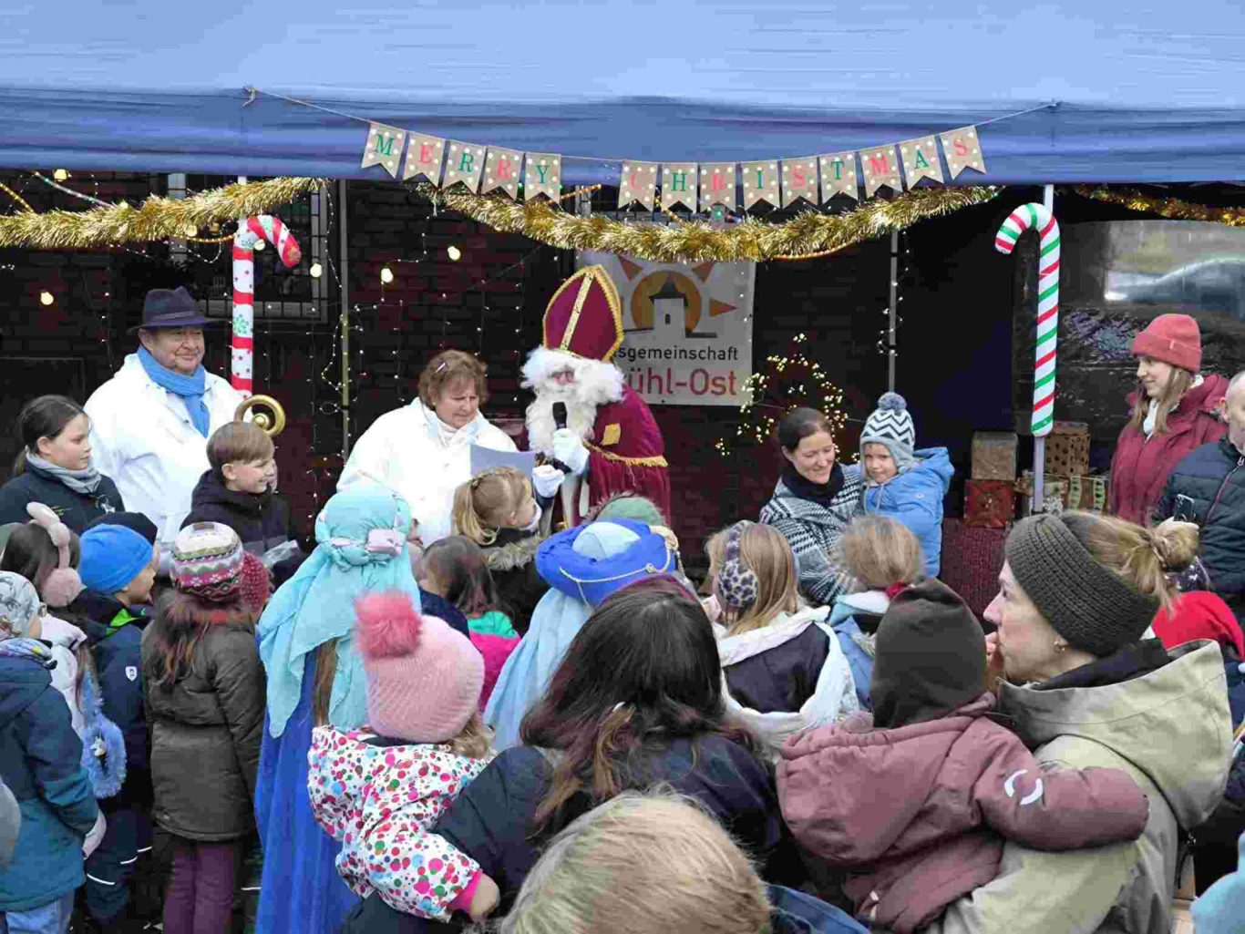 Weihnachtsmarkt Ortsgemeinschaft Brühl-Ost 2025 auf dem Vorplatz St. Stephan Eine Menschenmenge um einen festlich geschmückten Stand mit einem verkleideten Weihnachtsmann.