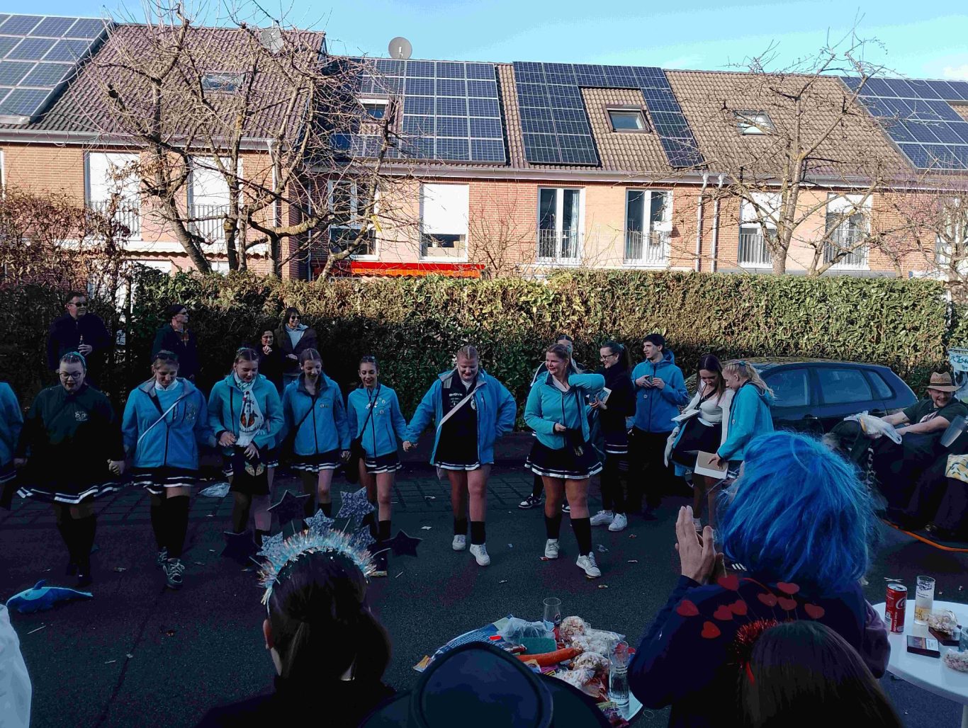 Karnevalszug in Brühl-Ost 2026 Gruppenszene mit Tänzern in blauen Jacken, Menschen im Hintergrund, sonniger Tag.